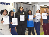 A group of emergency department employees holds up pieces of paper displaying their names and job titles.